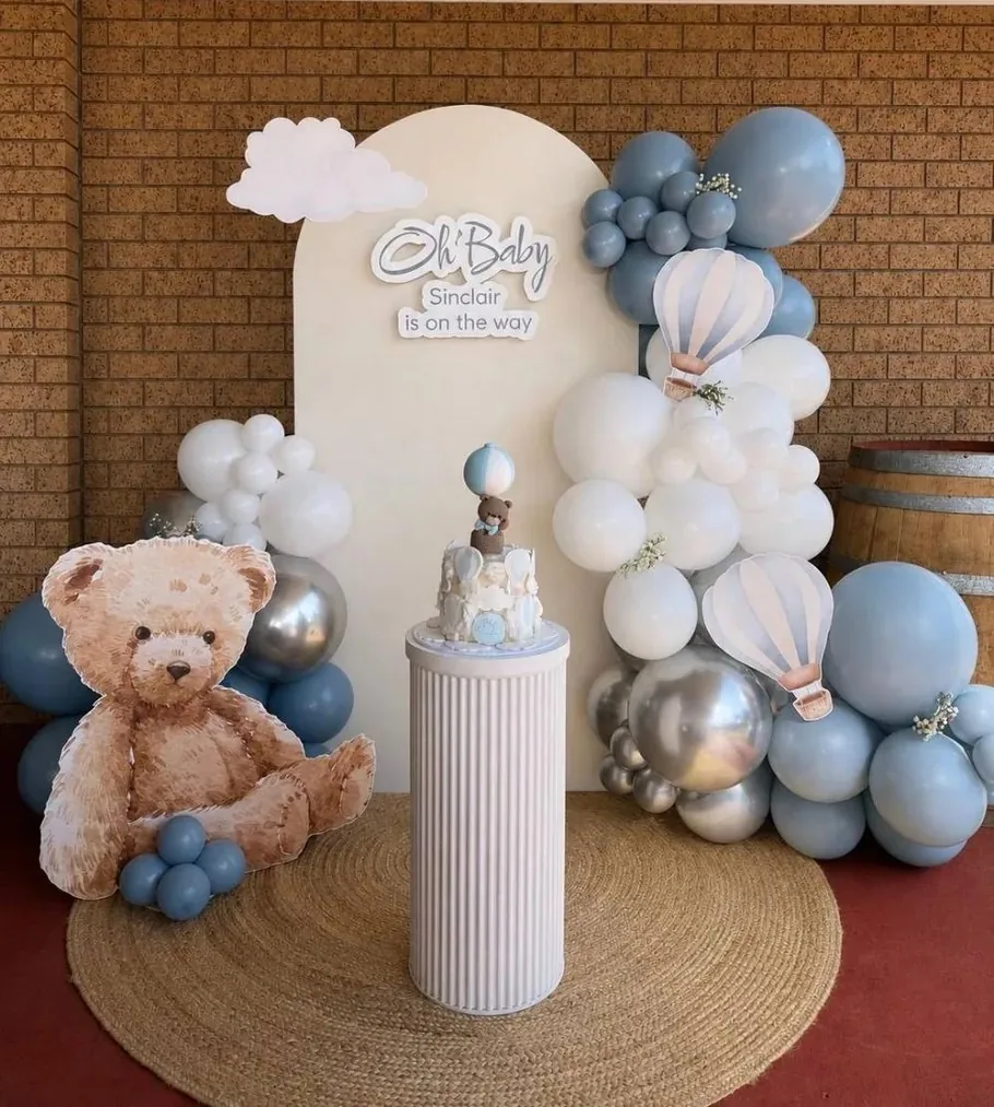 Blue balloon baby shower backdrop with a teddy bear cut-out and cake plinth